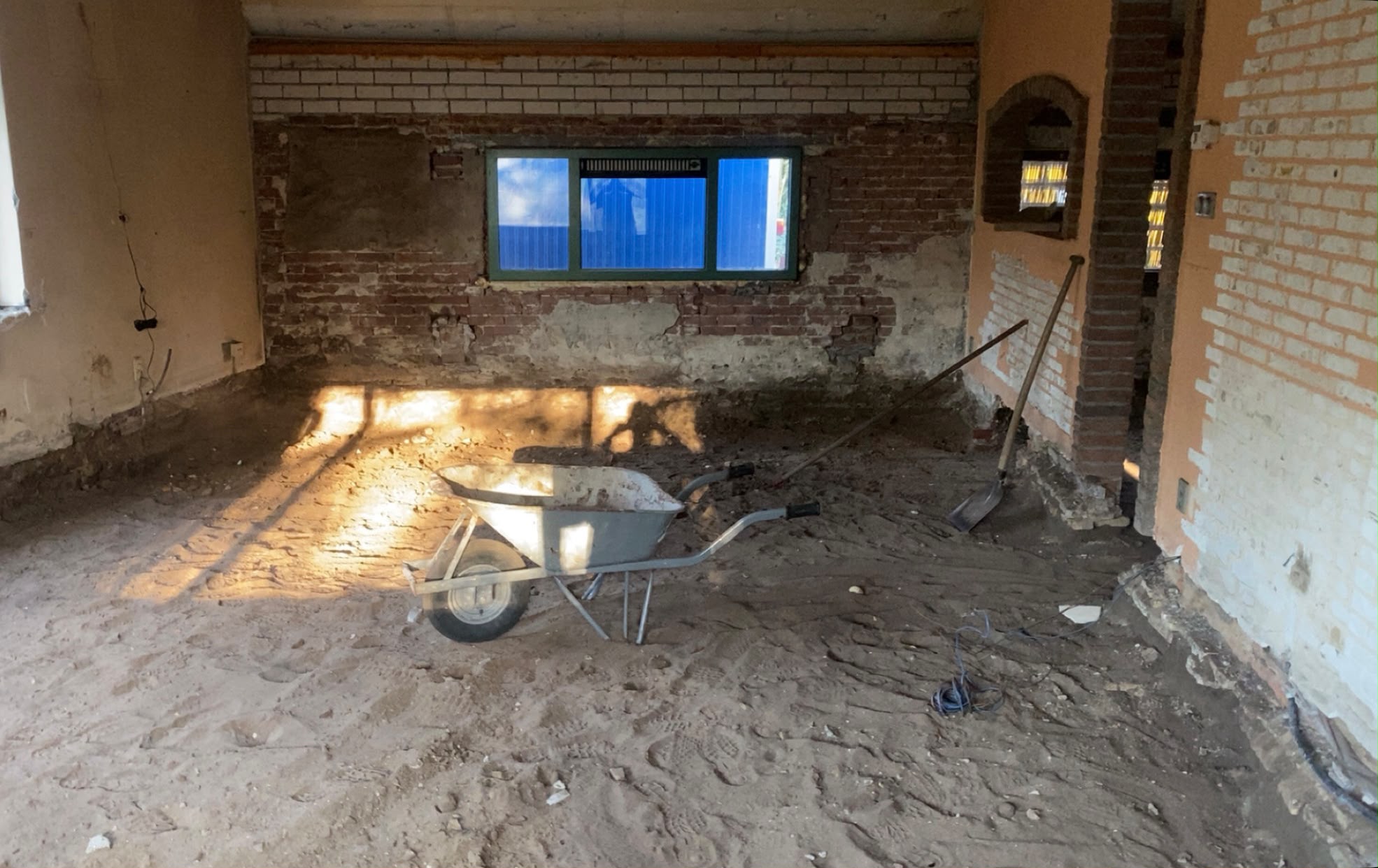 Woonkamer in Onna gesloopt tot op het zandbed, met kale bakstenen muren en kruiwagen